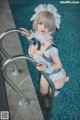 A woman in a maid outfit leaning on a railing by a pool.