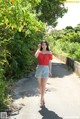 A woman in a red top and denim shorts walking down a path.