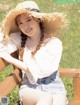 A woman sitting on a wooden bench wearing a straw hat.