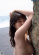 A naked woman leaning against a rock on the beach.