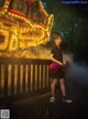 A woman standing in front of a carousel at night.